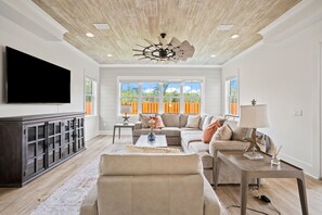 A living room with a large flat-screen TV, a ceiling fan, a sectional sofa, and a coffee table. - Quiet Street. 0.6 miles from beach. Private Pool/Grill/Bikes. (Santa Rosa Beach)