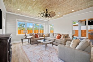 A spacious living room with a ceiling fan, large windows, and a view of the outdoors. - Quiet Street. 0.6 miles from beach. Private Pool/Grill/Bikes. (Santa Rosa Beach)