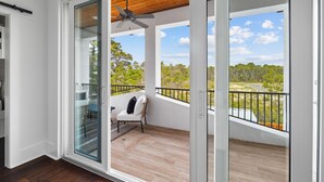 Un balcone con ventilatore a soffitto, una sedia e vista su un paesaggio verde.