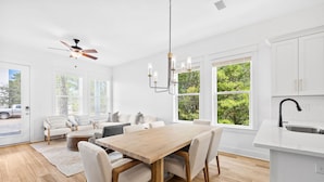 A modern kitchen with white cabinets, a wooden dining table, and a built-in island with a sink. - Dune Allen/30A! Access to Pool, walk to Beach/Stinky's! (Santa Rosa Beach)