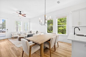 A modern kitchen with white cabinets, a wooden dining table, and a built-in island with a sink. - Dune Allen/30A! Access to Pool, walk to Beach/Stinky's! (Santa Rosa Beach)