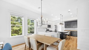 A modern kitchen with white cabinets, a wooden dining table, and a view of greenery outside. - Dune Allen/30A! Access to Pool, walk to Beach/Stinky's! (Santa Rosa Beach)