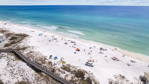 A beach with a wooden boardwalk leading to a white building, clear blue water, and a sandy shore. - Dune Allen/30A! Access to Pool, walk to Beach/Stinky's! (Santa Rosa Beach)