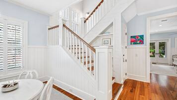 A spacious room with a wooden staircase, white walls, and a dining area with a table and chairs.