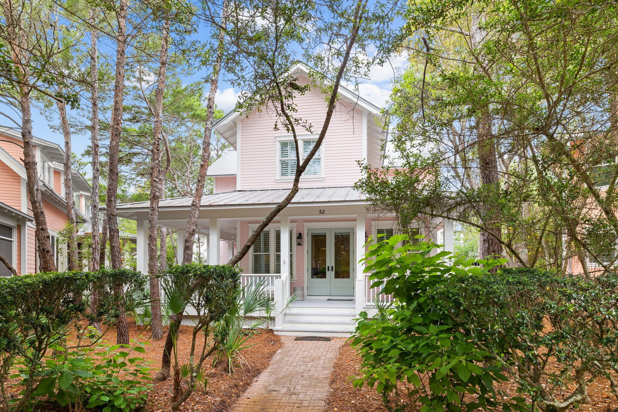 A two-story house with a porch, surrounded by trees and a brick pathway.