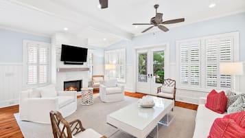 A spacious living room with a fireplace, white furniture, and a ceiling fan.