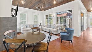 A spacious living area with a wooden ceiling, a round dining table, and a blue armchair. - Golf Cart/Bikes! Dune Allen/Walk to beach! (Santa Rosa Beach)