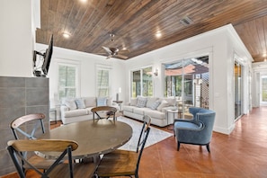 A spacious living area with a wooden ceiling, a round dining table, and a blue armchair. - Golf Cart/Bikes! Dune Allen/Walk to beach! (Santa Rosa Beach)