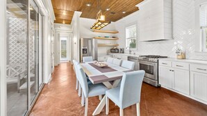 A modern kitchen with white cabinetry, a central island, and a dining area with a large table and chairs. - Golf Cart/Bikes! Dune Allen/Walk to beach! (Santa Rosa Beach)