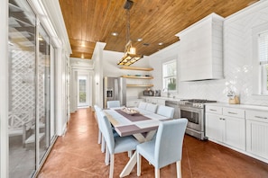 A modern kitchen with white cabinetry, a central island, and a dining area with a large table and chairs. - Golf Cart/Bikes! Dune Allen/Walk to beach! (Santa Rosa Beach)
