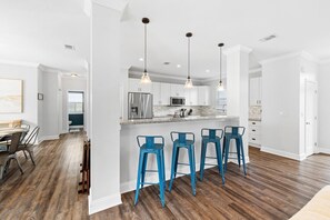 A modern kitchen with white cabinets, a stainless steel refrigerator, and blue bar stools. - Pet Friendly! Golf Cart/Bikes! Ride to Beach/Resort Pool! (Santa Rosa Beach)
