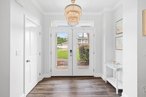 A hallway with a wooden floor, white walls, a chandelier, and a door leading outside. - Pet Friendly! Golf Cart/Bikes! Ride to Beach/Resort Pool! (Santa Rosa Beach)