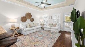 A spacious living room with a ceiling fan, white sofas, a colorful rug, and a large plant. - Golf Cart/Bikes! Dune Allen 30A. Pool Access. (Santa Rosa Beach)
