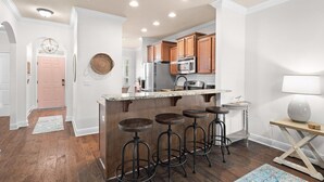 A modern kitchen with wooden cabinets, a stainless steel refrigerator, and a bar area with stools. - Golf Cart/Bikes! Dune Allen 30A. Pool Access. (Santa Rosa Beach)
