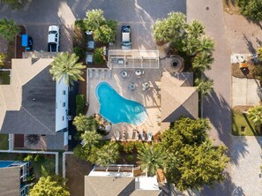 Vue aérienne d’un hôtel doté d’une piscine, d’un espace de détente en plein air et de palmiers.