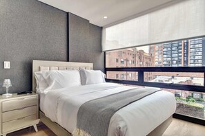 Ein modernes Schlafzimmer mit großem Fenster, einem Bett mit weißer Bettwäsche, einem Nachttisch und einer Lampe.