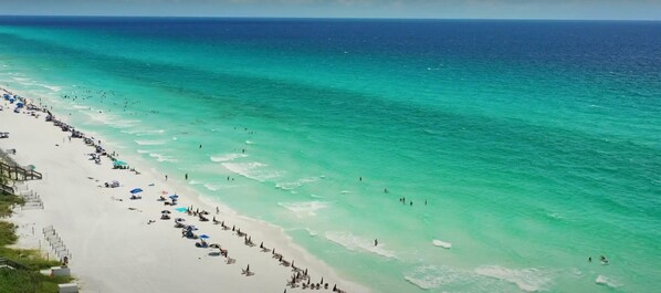 A beach with clear turquoise water, white sand, and a long stretch of beach with umbrellas and people. - Gulf Place 30A! Walk to Beach. (SANTA ROSA BEACH)