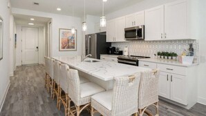 A modern kitchen with white cabinetry, a large island with bar stools, stainless steel appliances, and pendant lighting. - Gulf Place 30A! Walk to Beach. (SANTA ROSA BEACH)