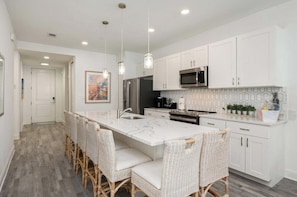 A modern kitchen with white cabinetry, a large island with bar stools, stainless steel appliances, and pendant lighting. - Gulf Place 30A! Walk to Beach. (SANTA ROSA BEACH)