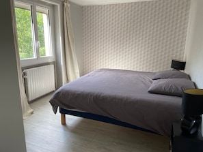 Une chambre à coucher avec un lit, un radiateur, une fenêtre avec des rideaux et une lampe.