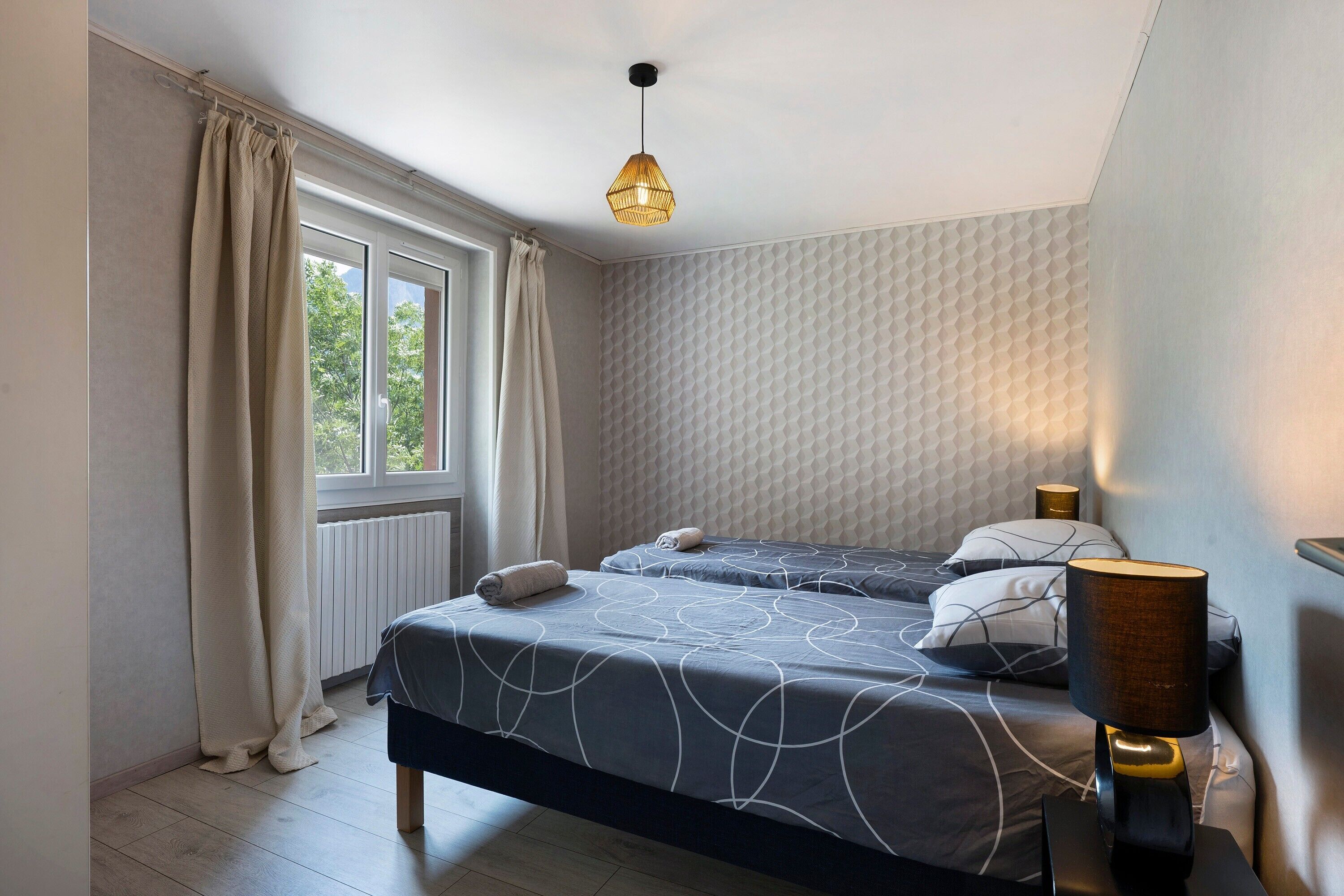 Ein Schlafzimmer mit zwei Betten, einem Fenster, einer Heizung und einer Pendelleuchte.