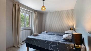 Ein Schlafzimmer mit zwei Betten, einem Fenster, einer Heizung und einer Pendelleuchte.