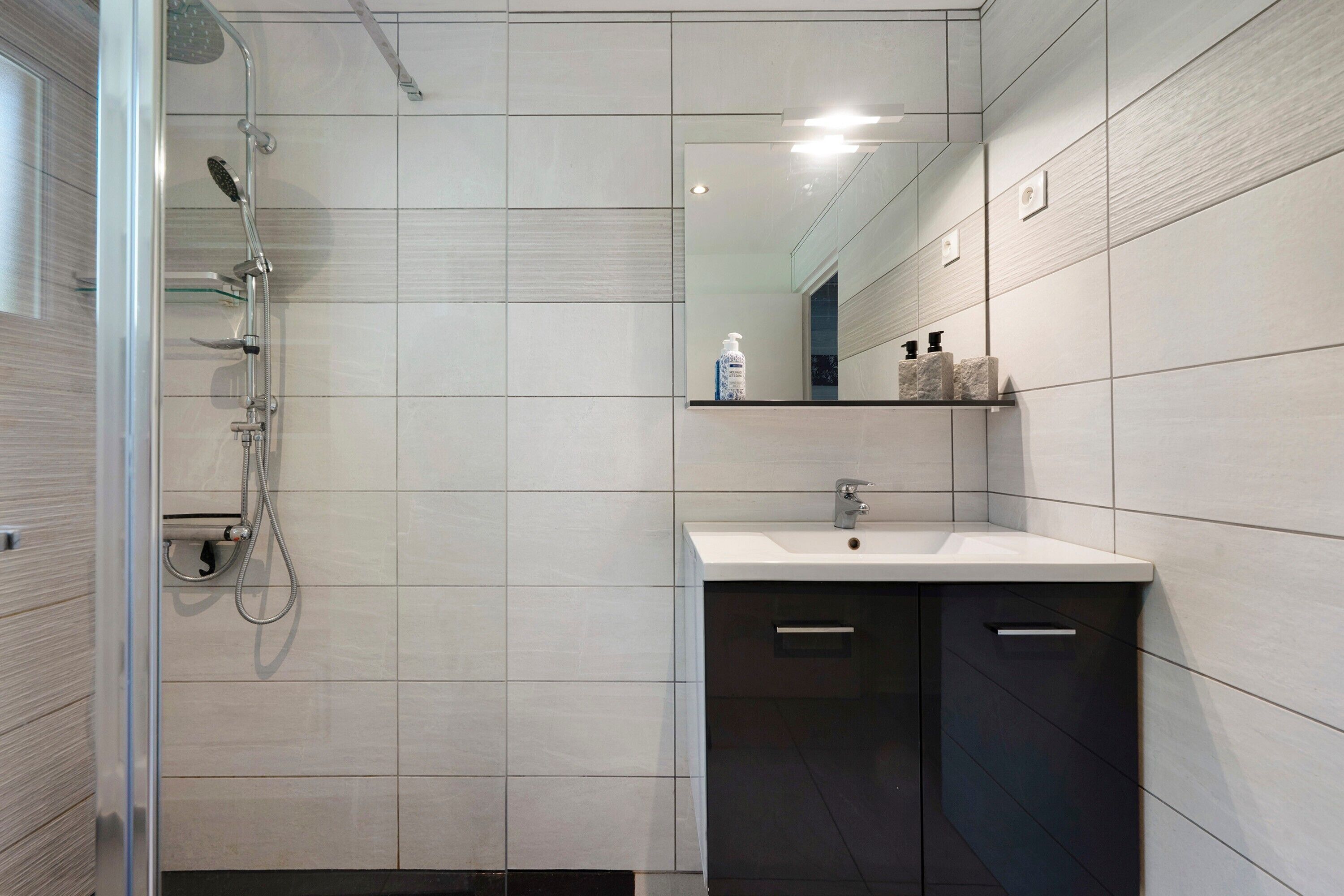 Un baño moderno con ducha, lavamanos y espejo.