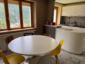 Une cuisine avec un coin repas, une fenêtre donnant sur un espace verdoyant et un radiateur.