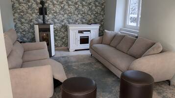 En stue med pejs, sofa, to fodskamler og tapet med mønster.