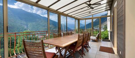Un área de comedor techada al aire libre con una mesa y sillas, con vista a un paisaje montañoso.