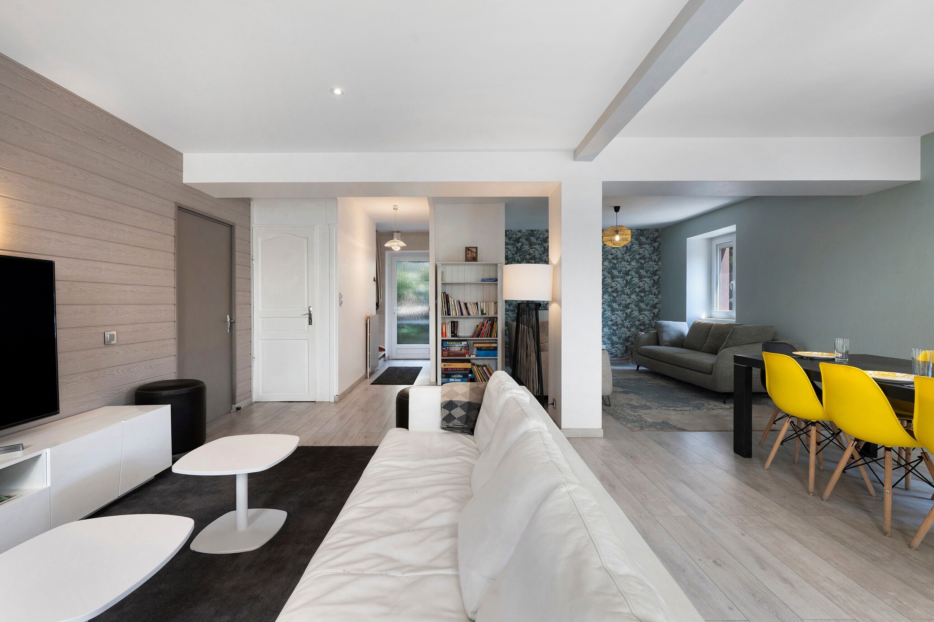 Un salon moderne avec un canapé blanc, un téléviseur à écran plat et un coin repas doté de chaises jaunes.