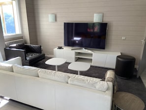 Ett modernt vardagsrum med en vit soffa, en svart läderfåtölj, en platt-TV och ett litet vitt soffbord.