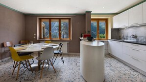 A modern kitchen with white cabinets, a central island, and a dining area with chairs and a table.