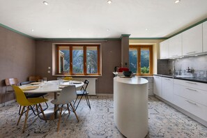 Cocina moderna con armarios blancos, una isla central y un comedor con sillas y una mesa.