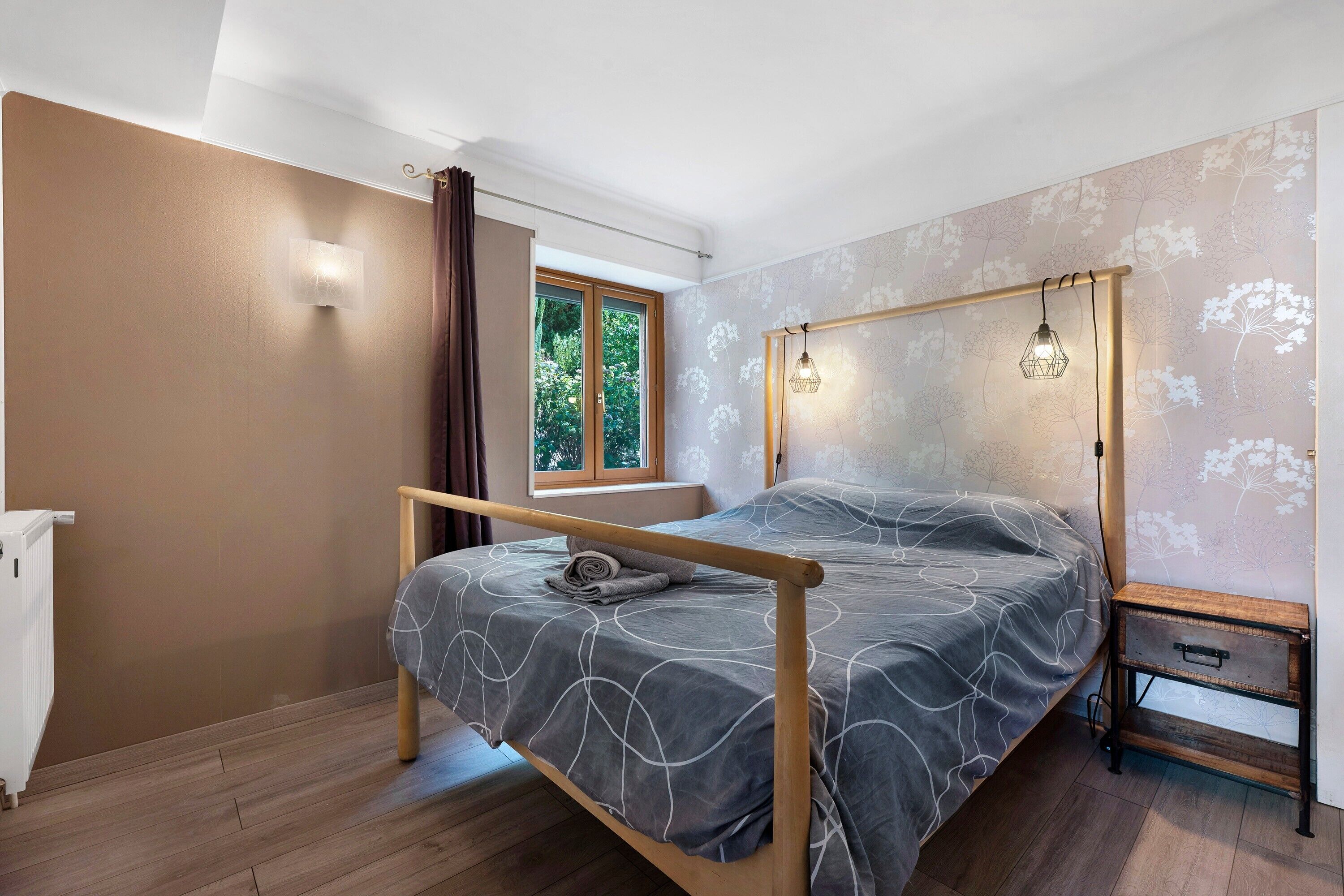 A bedroom with a bed, a window, a radiator, and a wooden floor.