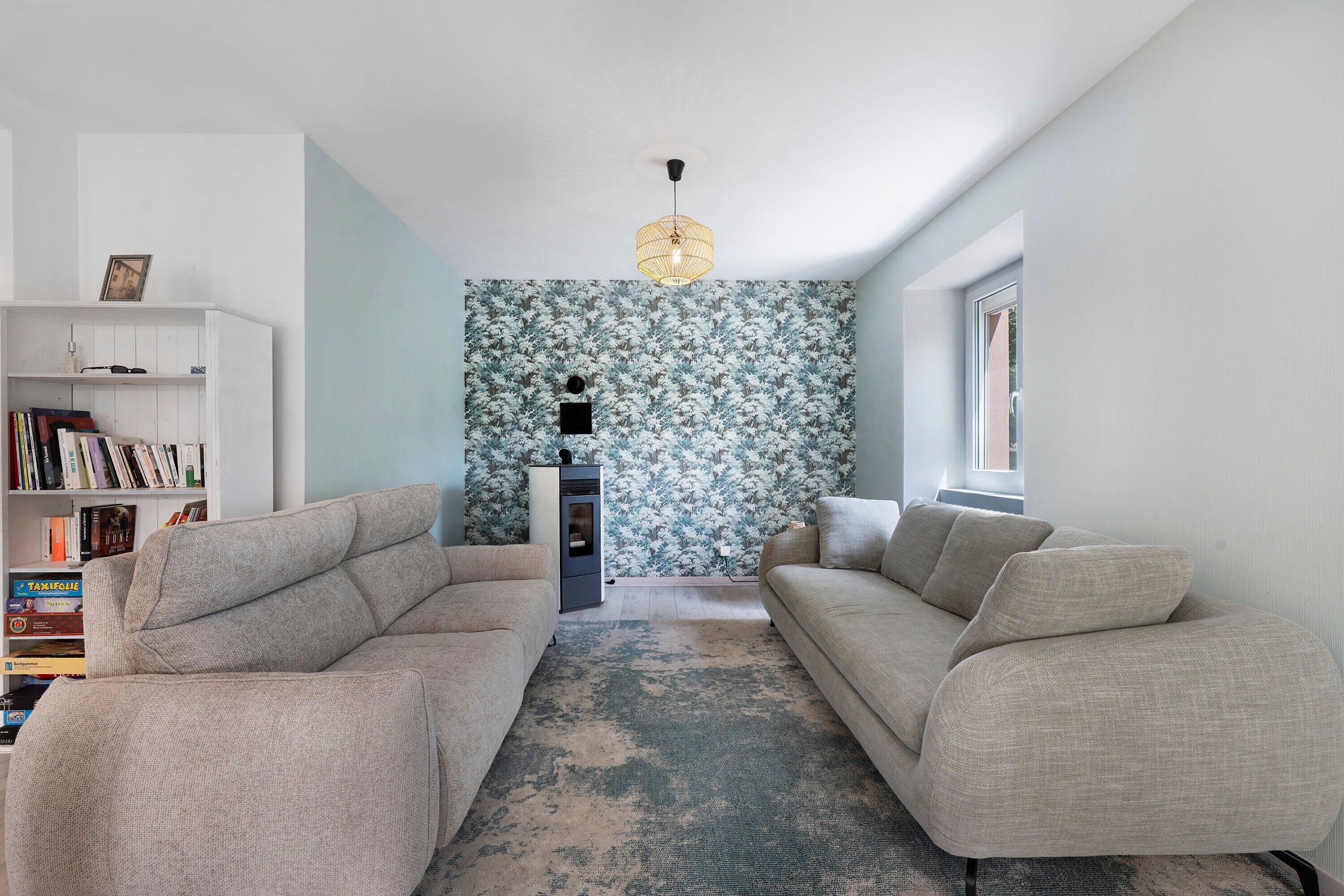 En moderne stue med en sofasæt, en bogreol og tapet med et mønster.