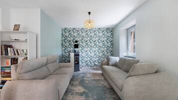 A modern living room with a sofa set, a bookshelf, and a patterned wallpaper.