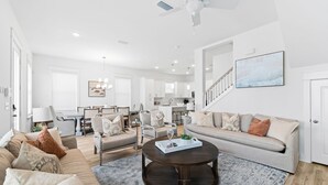 A spacious living room with a dark wooden coffee table, beige sofas, and a staircase leading to an upper level. - Dune Allen/30A! Walk to Beach/Coffee/Dinner! Bikes! (Santa Rosa Beach)