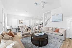 A spacious living room with a dark wooden coffee table, beige sofas, and a staircase leading to an upper level. - Dune Allen/30A! Walk to Beach/Coffee/Dinner! Bikes! (Santa Rosa Beach)