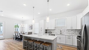 A modern kitchen with white cabinets, a marble backsplash, and a central island with bar stools. - Dune Allen/30A! Walk to Beach/Coffee/Dinner! Bikes! (Santa Rosa Beach)