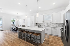 A modern kitchen with white cabinets, a marble backsplash, and a central island with bar stools. - Dune Allen/30A! Walk to Beach/Coffee/Dinner! Bikes! (Santa Rosa Beach)