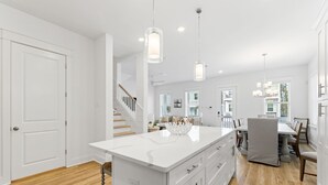 A modern kitchen with white cabinetry, a central island, pendant lighting, and a view to the dining area. - Dune Allen/30A! Walk to Beach/Coffee/Dinner! Bikes! (Santa Rosa Beach)