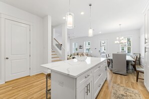 A modern kitchen with white cabinetry, a central island, pendant lighting, and a view to the dining area. - Dune Allen/30A! Walk to Beach/Coffee/Dinner! Bikes! (Santa Rosa Beach)