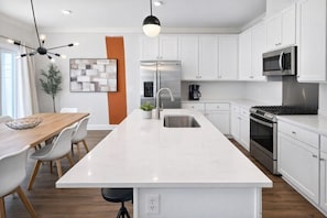 A modern kitchen with white cabinetry, stainless steel appliances, and a central island with seating.