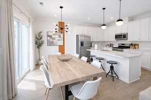 Een moderne keuken met witte kasten, een houten eettafel en barkrukken.