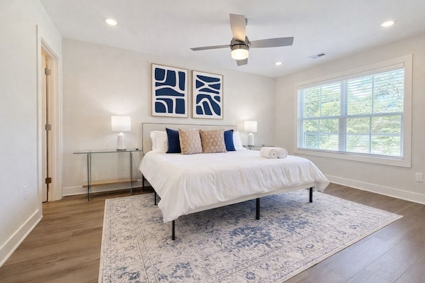 A bedroom with a bed, a ceiling fan, a window, and artwork on the wall.