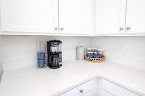 Una cocina con armarios blancos, una cafetera y una cesta con frascos.