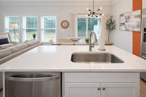 A modern kitchen with a large island, stainless steel appliances, and a dining area with a sofa and table.