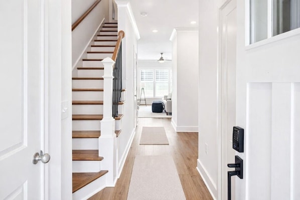 A hallway with a wooden staircase, a rug, and a door with a keypad lock.
