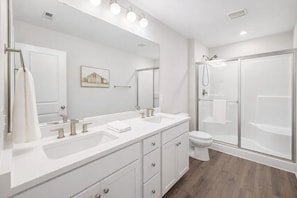 Een moderne badkamer met een grote spiegel, twee wasbakken, een toilet en een douche met glazen wanden.